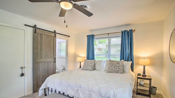 A bedroom with a bed, a nightstand, a ceiling fan, a window with curtains, and a door with a sliding barn door. - 1 Mi to Main St: Brenham Retreat w/ Game Room (Brenham)