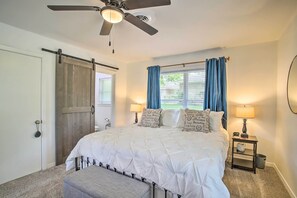 A bedroom with a bed, a nightstand, a ceiling fan, a window with curtains, and a door with a sliding barn door. - 1 Mi to Main St: Brenham Retreat w/ Game Room (Brenham)