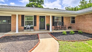 A brick house with a covered porch, a front door with a wreath, and a small seating area with chairs. - 1 Mi to Main St: Brenham Retreat w/ Game Room (Brenham)
