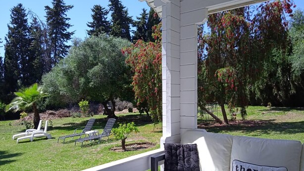 A covered outdoor seating area with a white sofa and two lounge chairs, a small table, and a decorative pillow with a quote.