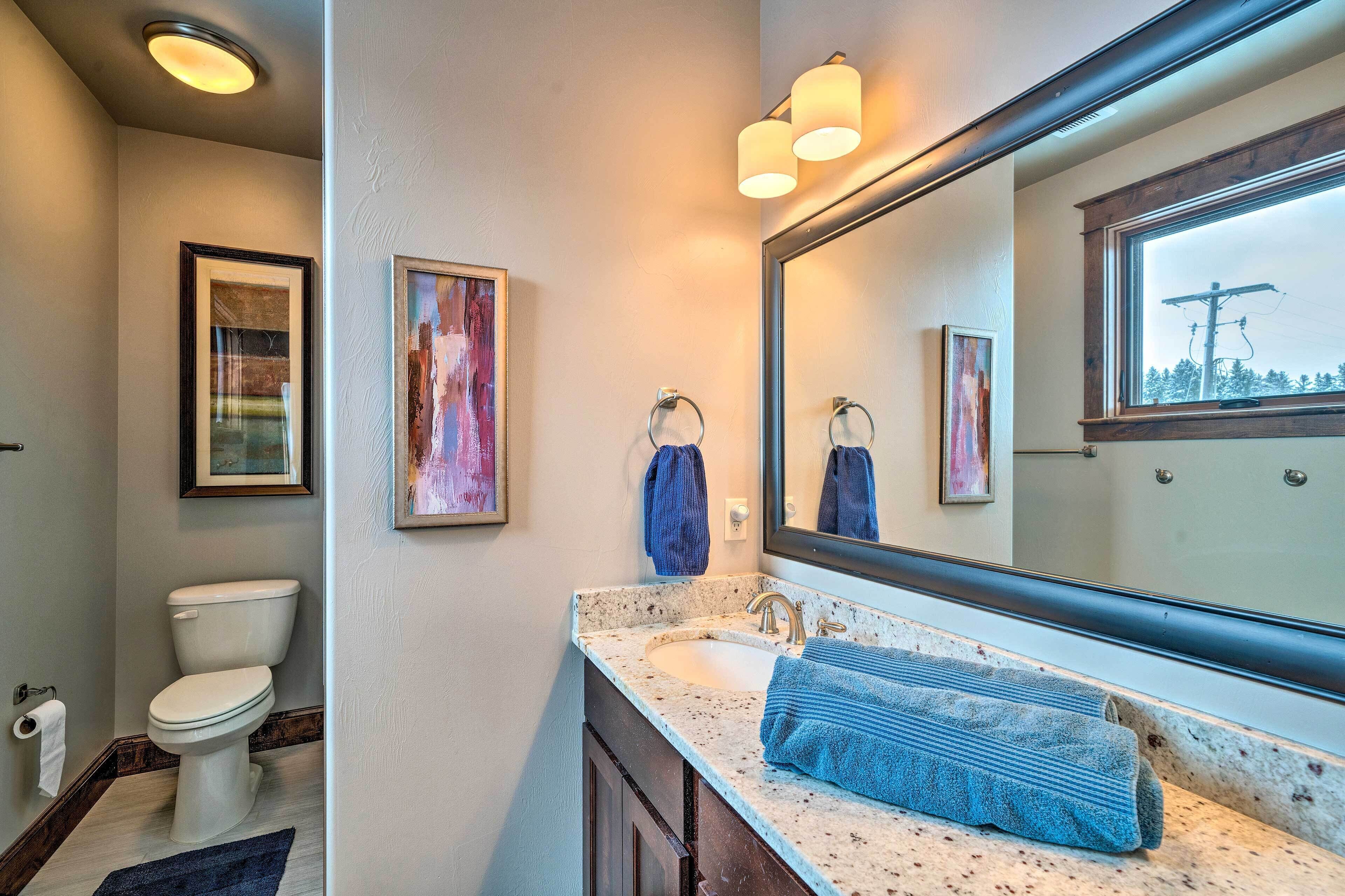 A bathroom with a toilet, sink, and large mirror. There are towels hanging on the wall and a framed picture above the mirror.