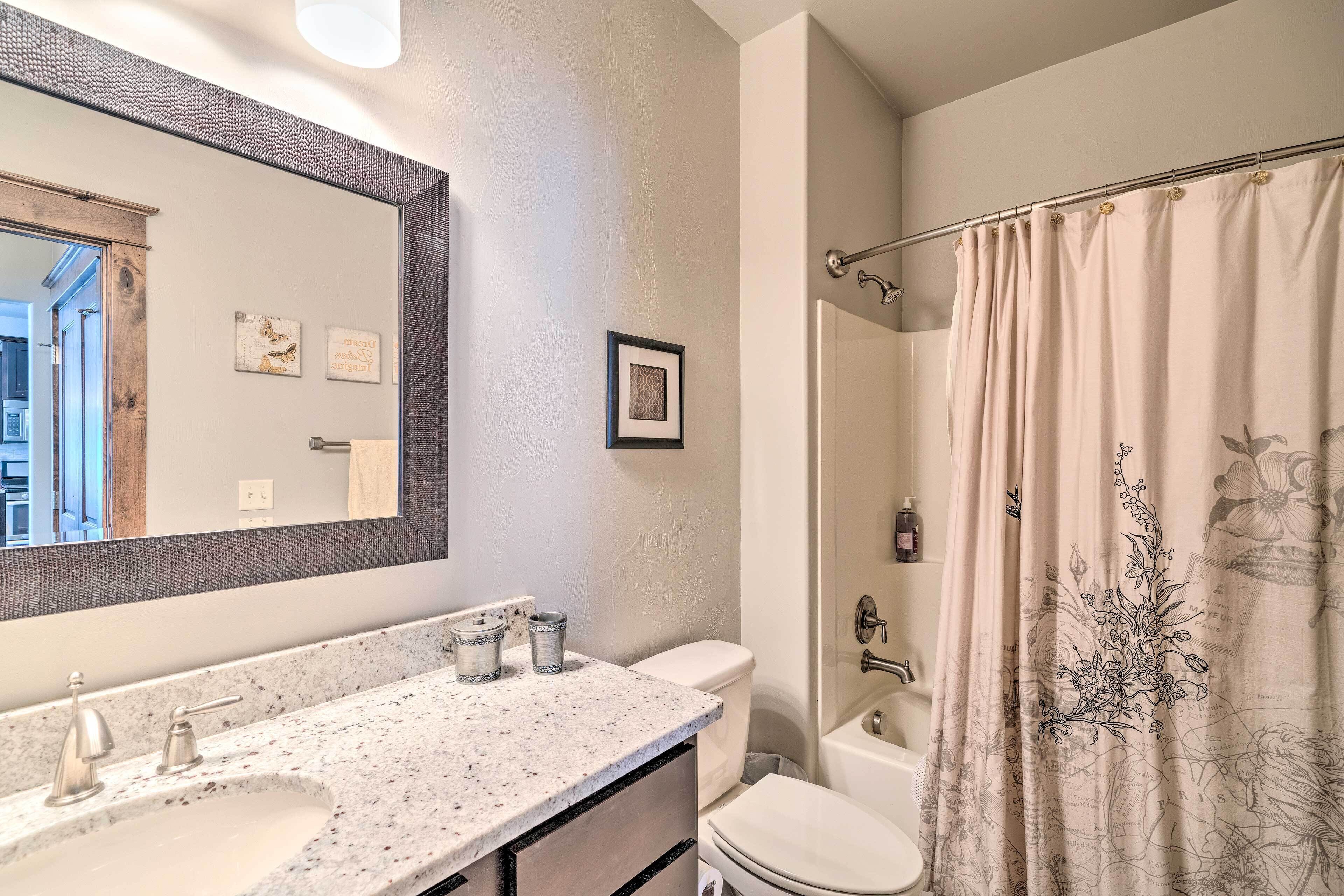 A bathroom with a large mirror, a sink with a marble countertop, a toilet, and a shower curtain with a floral design.