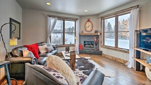 A cozy living room with a leather sofa, a fireplace, and large windows offering a view of the outdoors. - Main St Bozeman Condo - Walk to Parks & Eateries! (Bozeman)