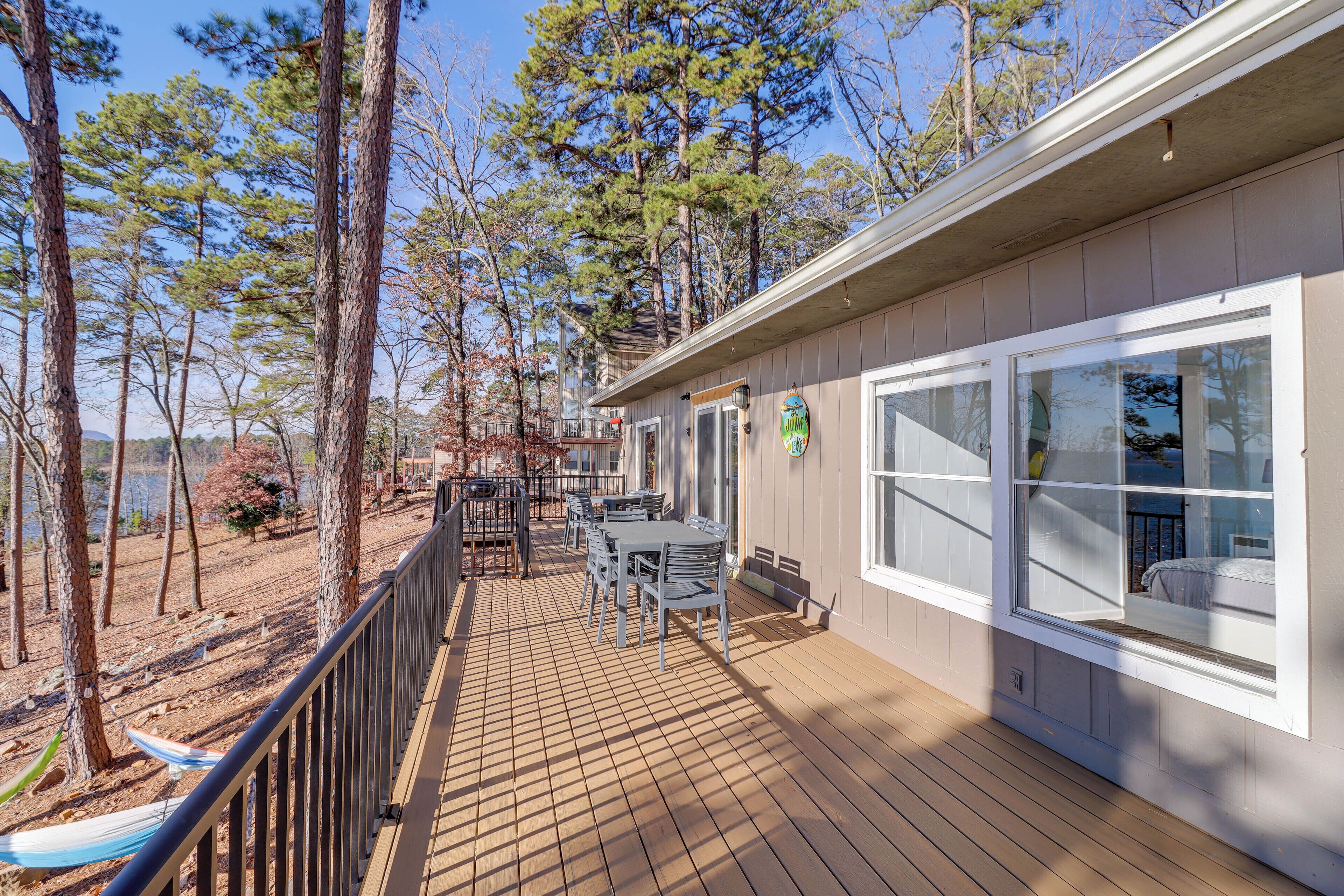 Une terrasse en bois avec des meubles d’extérieur, un hamac et une vue sur les arbres et un lac.