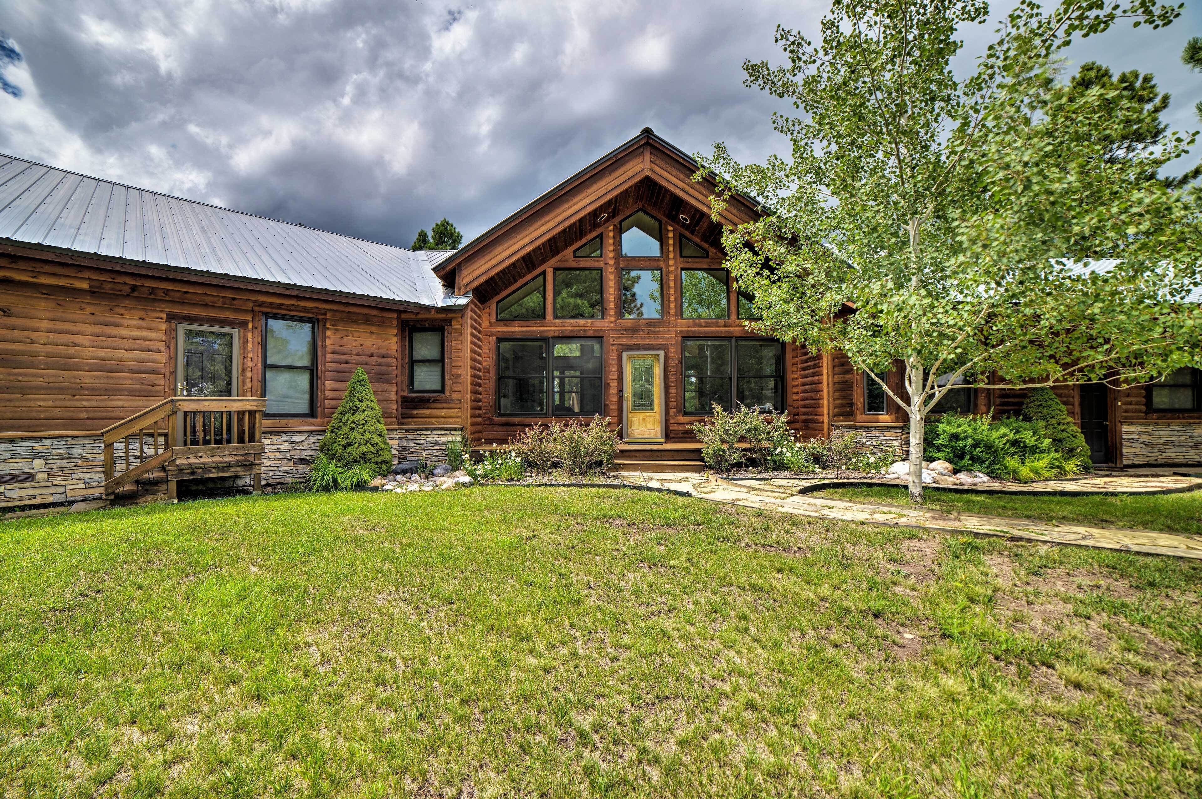 A log cabin with a stone foundation, large windows, and a well-maintained lawn.