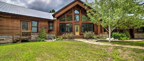 A log cabin with a stone foundation, large windows, and a well-maintained lawn.