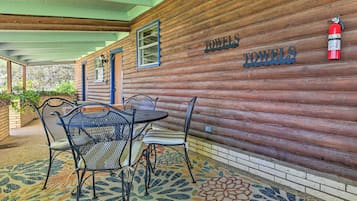 A wooden cabin with a covered patio area featuring a table and chairs, a fire extinguisher, and a sign that reads "TOWELS".