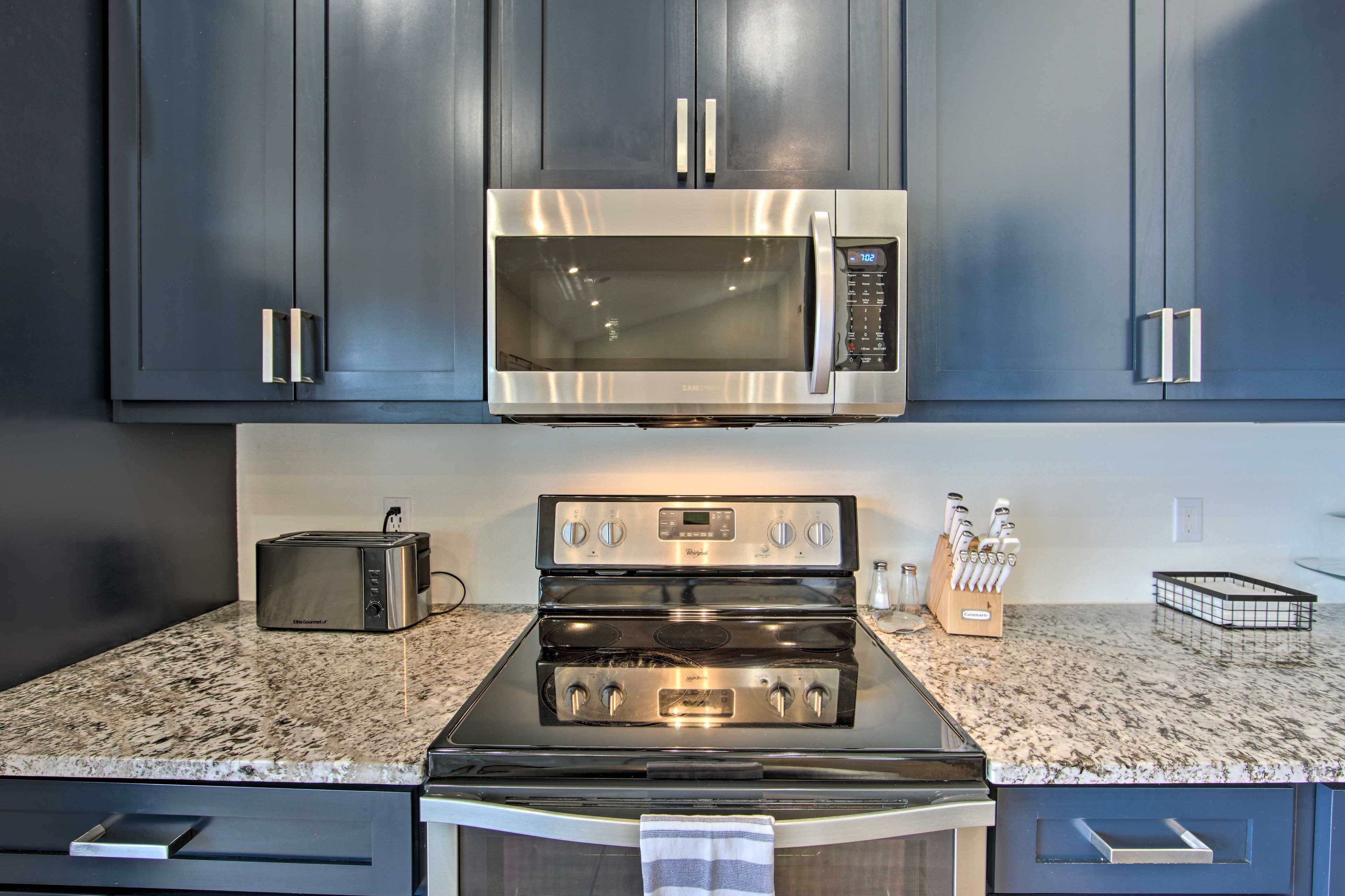 A kitchen with dark cabinets, a stainless steel microwave, a toaster, and a stove.