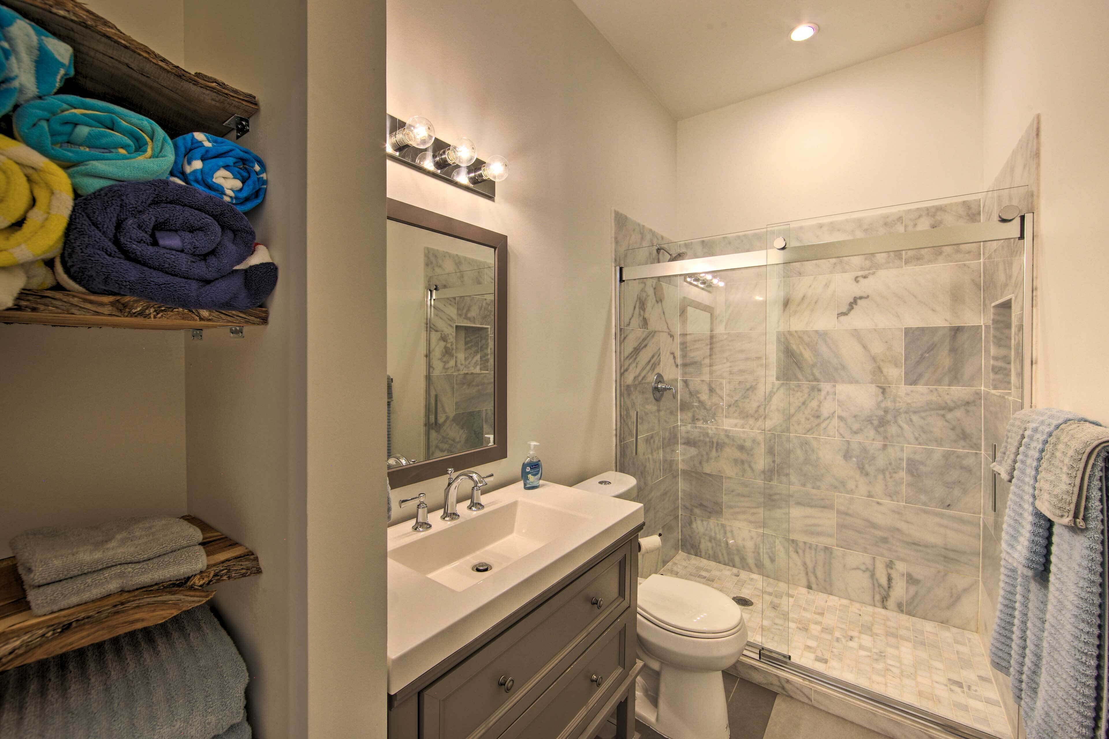 A modern bathroom with a glass-enclosed shower, marble tiles, a wooden vanity, and a mirror with lights.
