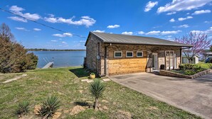 A small, two-story building with a stone facade and a wooden exterior, situated by a lake with a clear sky. - Modern Cedar Creek Lake Retreat w/ Panoramic View! (Malakoff)