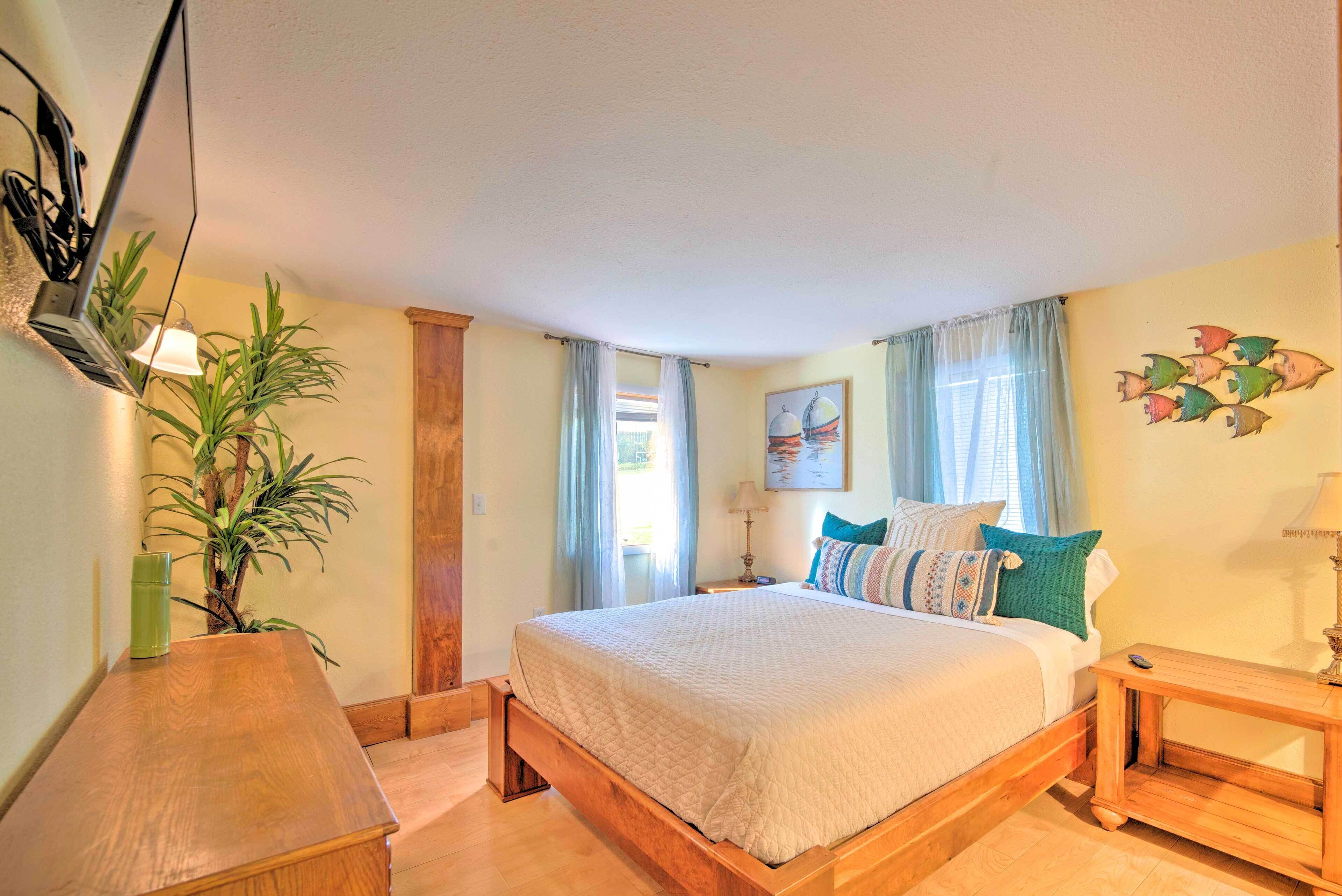 A bedroom with a wooden bed, a bedside table, a lamp, a plant, and a window with curtains.