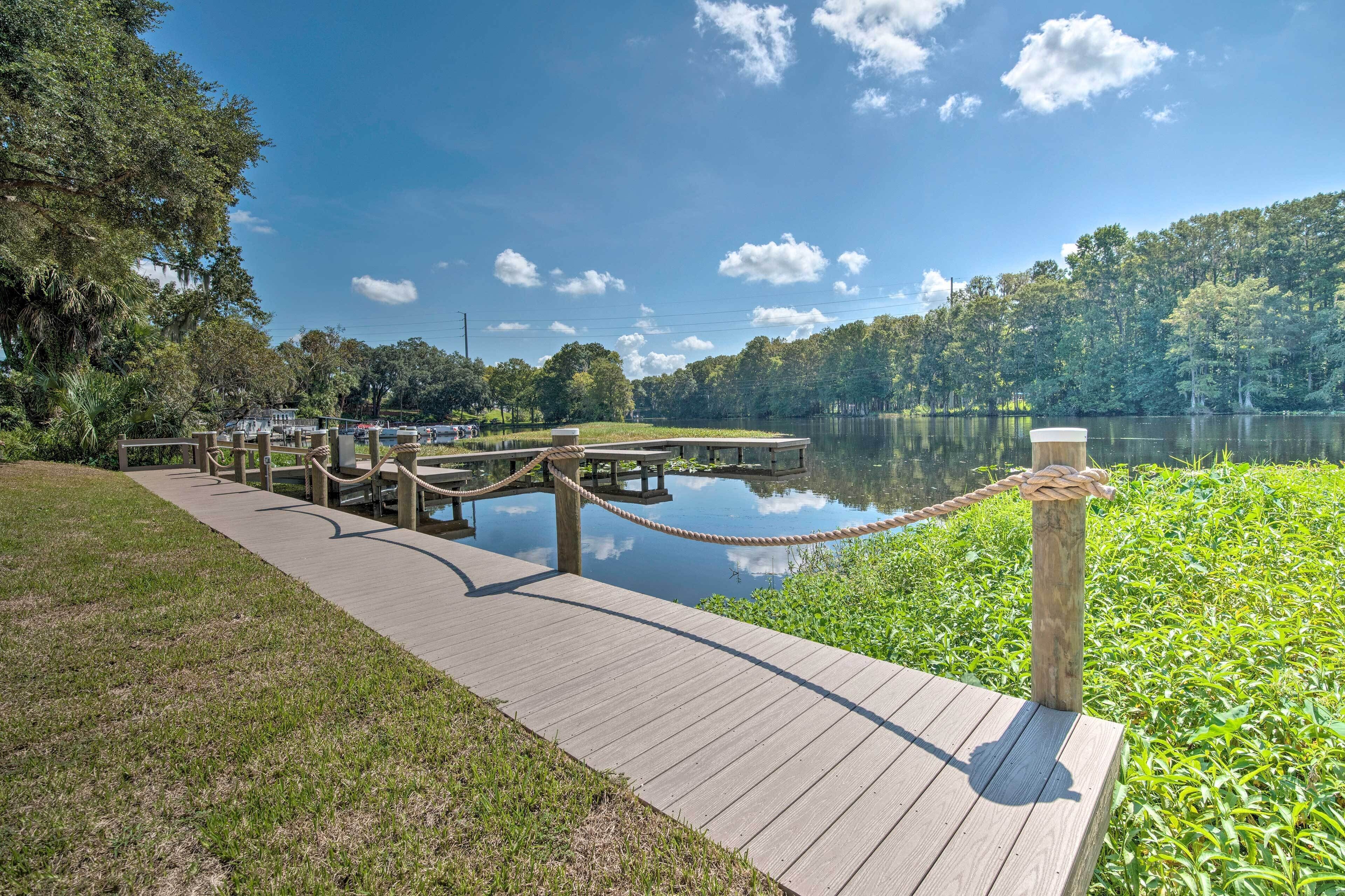 A wooden dock extending into a calm lake, surrounded by lush greenery and trees.