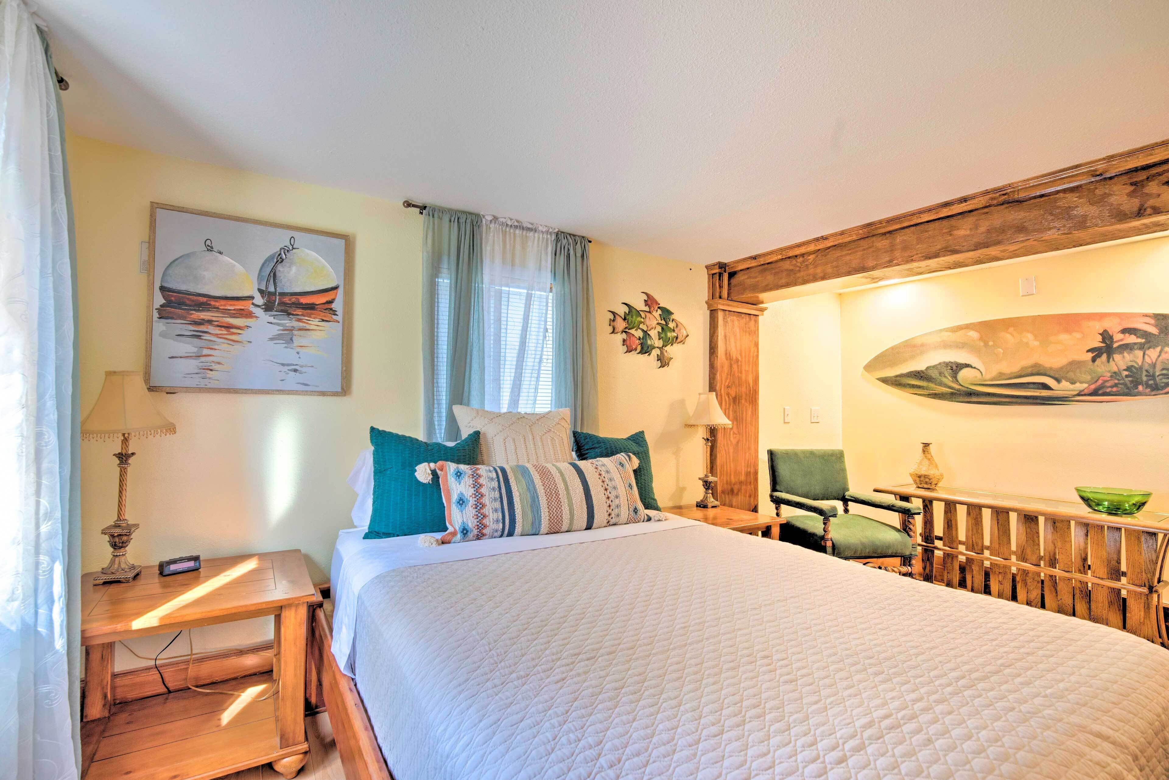 A neatly arranged bedroom with a bed, bedside table, lamp, chair, and artwork on the walls.