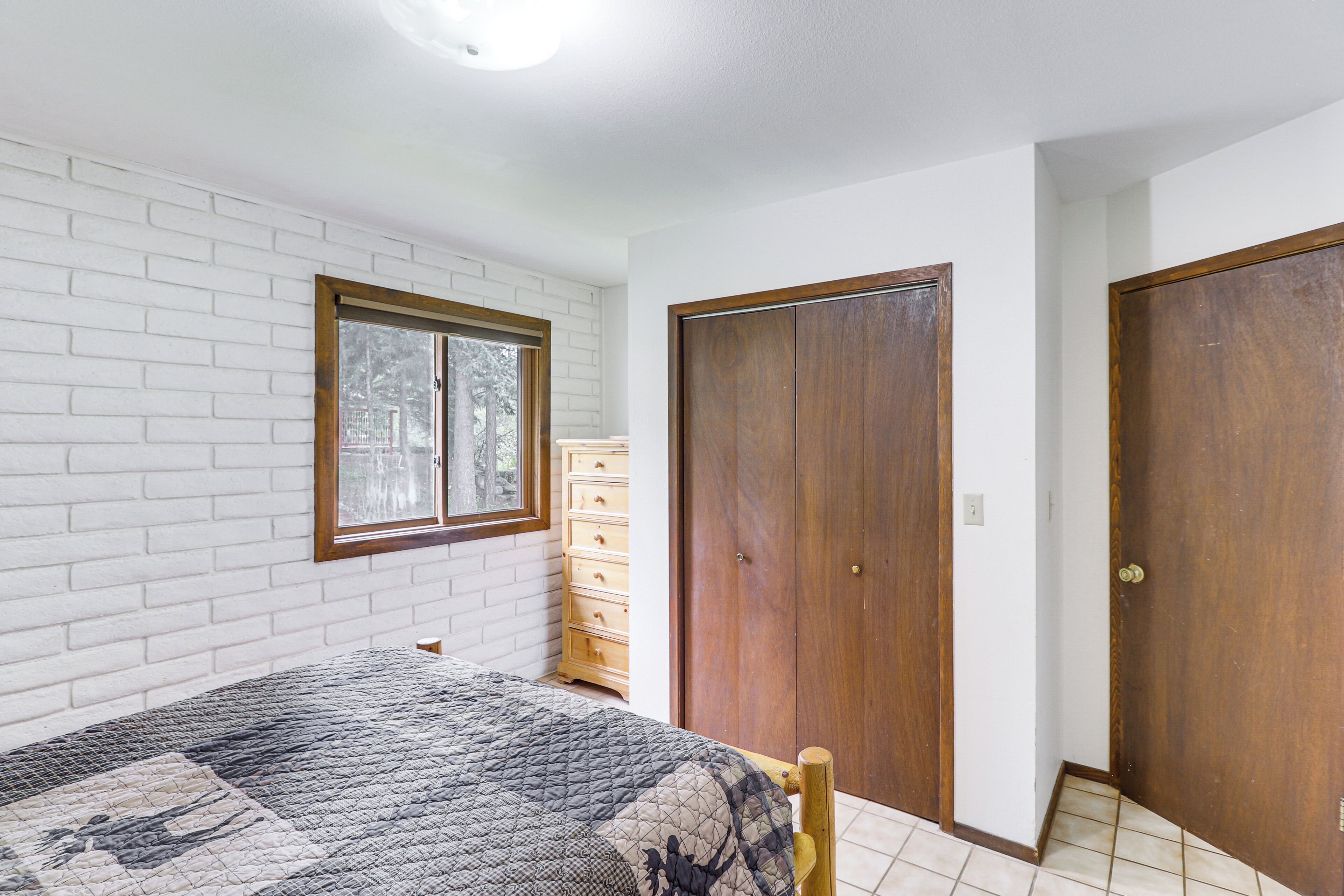 A bedroom with a bed, a dresser, a window, and two doors.
