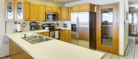 A kitchen with wooden cabinets, stainless steel appliances, a large island with a sink, and a view into the adjacent living area.