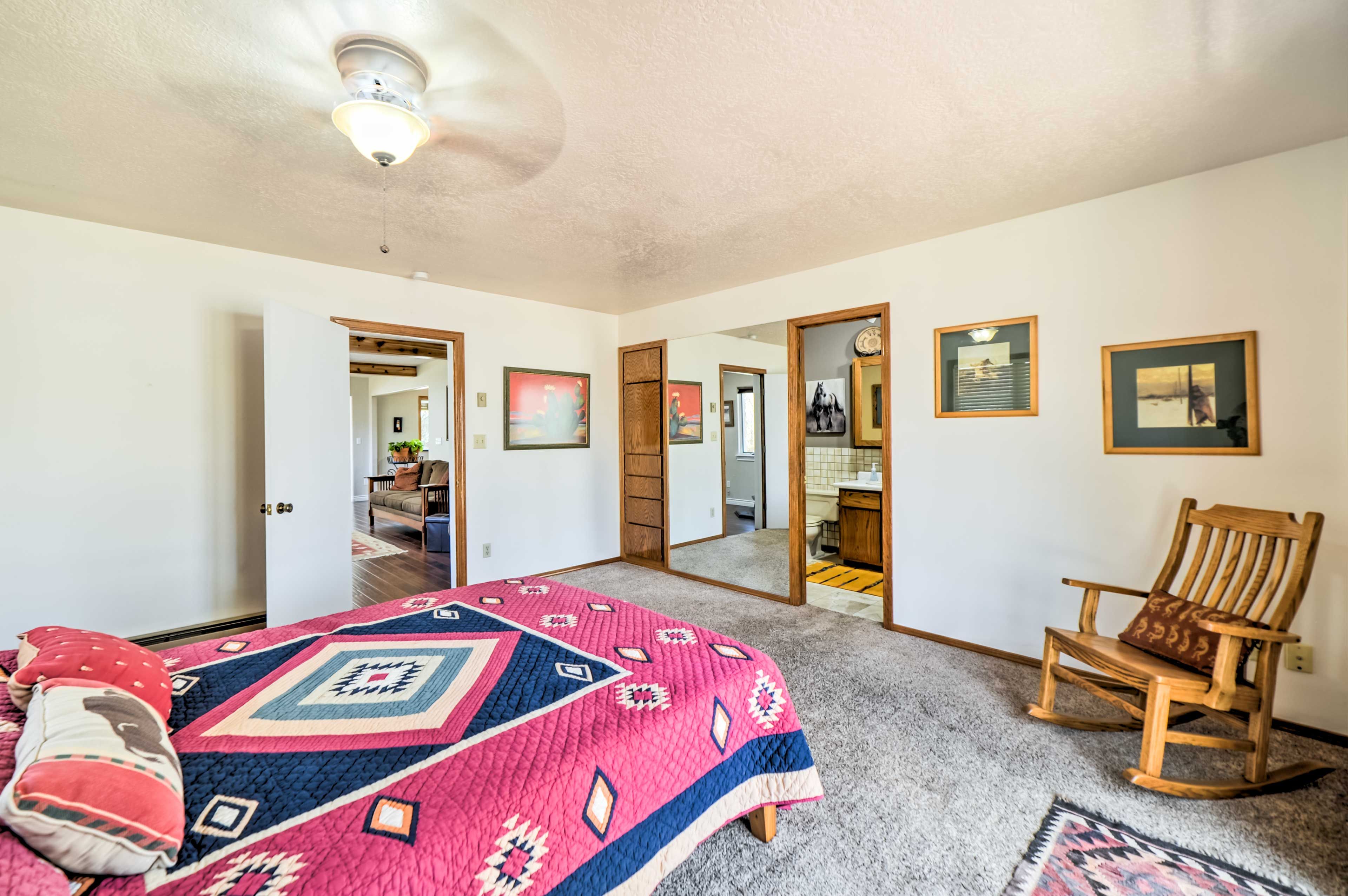 A bedroom with a large bed, a wooden rocking chair, and a door leading to another room.