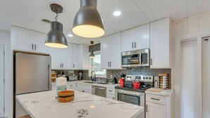 A modern kitchen with white cabinets, a marble island, stainless steel appliances, and pendant lighting. - Stylish Pensacola Retreat w/ Patio & Grill! (Pensacola)