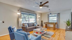 A living room with a sofa, armchairs, a coffee table, a foosball table, and a ceiling fan. - Stylish Pensacola Retreat w/ Patio & Grill! (Pensacola)