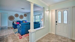 A spacious living room with a blue sofa set, a patterned rug, and a white column.