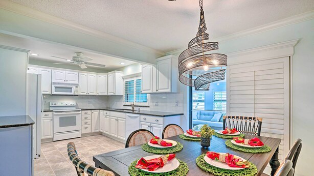 A modern kitchen with white cabinets, a dark wooden dining table set for four, and a unique hanging light fixture.