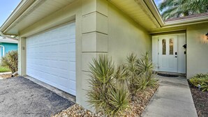 A residential garage with a white door, a small porch with a potted plant, and a concrete pathway leading to the door.