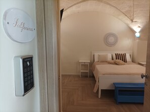 A bedroom with a bed, nightstands, a blue bench, a wall-mounted control panel, and a circular wall decoration.