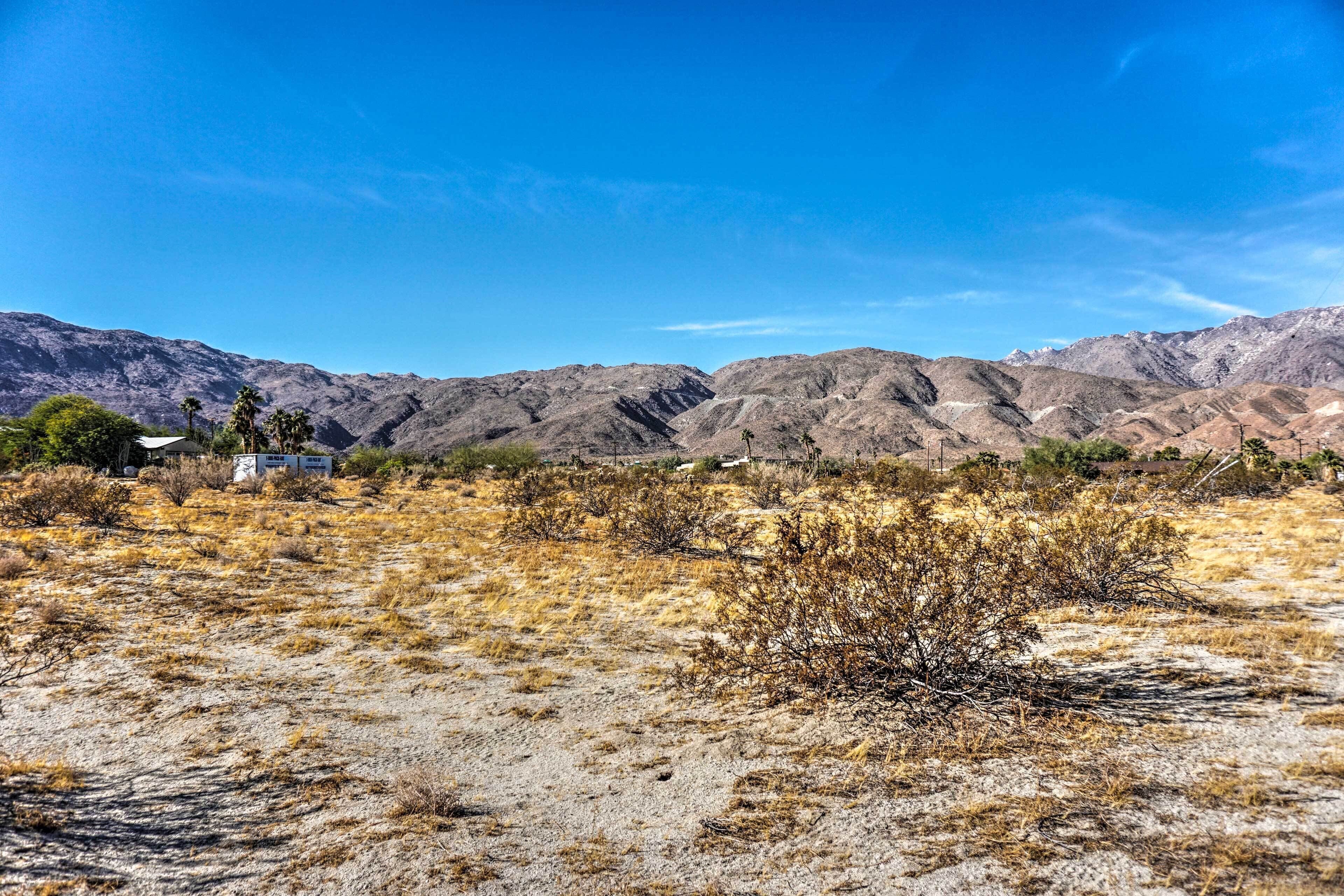 A desert landscape with mountains in the background, sparse vegetation, and a few buildings.