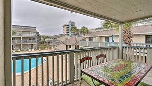 Ein Balkon mit Blick auf einen Swimmingpool, einem Tisch mit Stühlen und einer Palme.