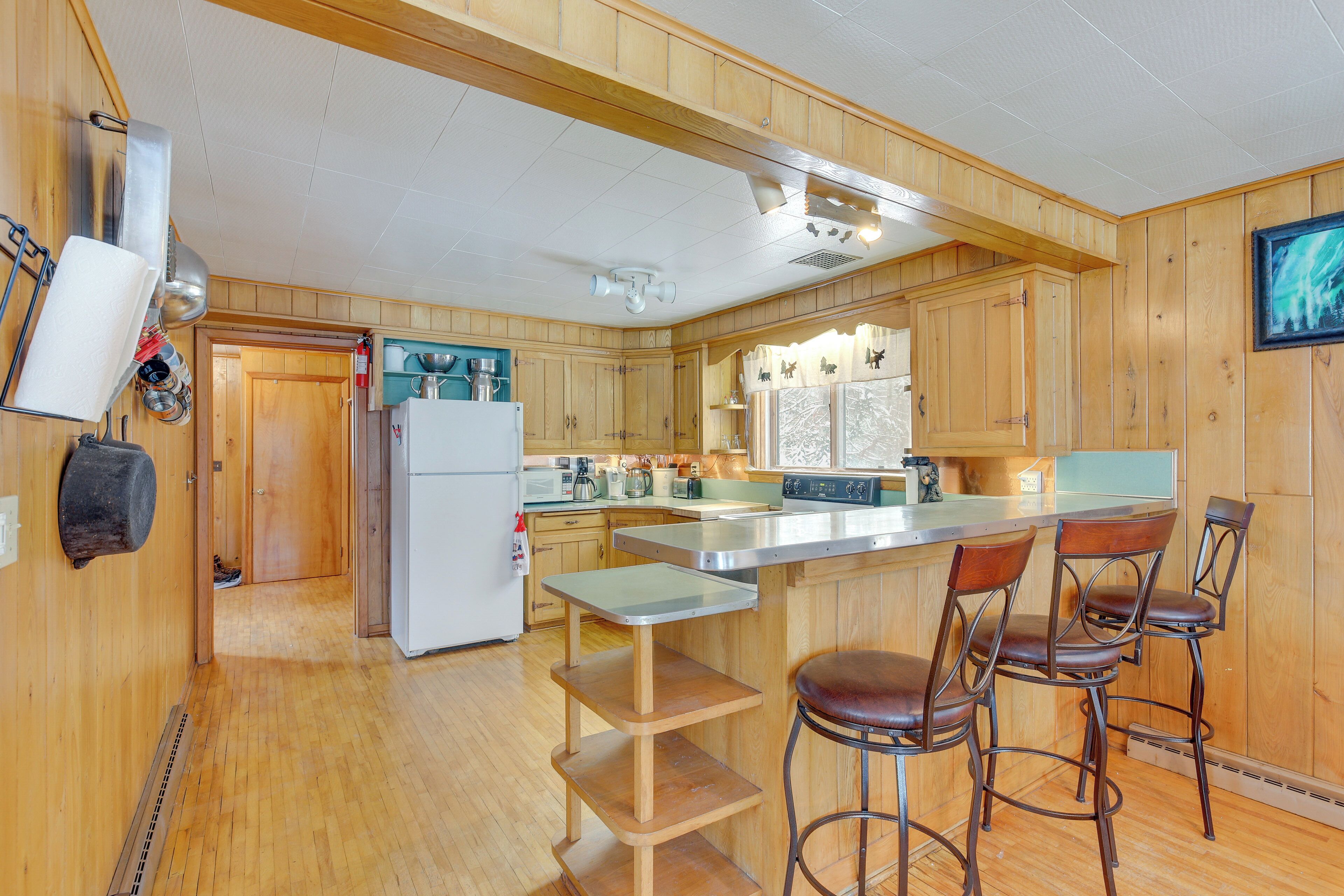 A wooden kitchen with a refrigerator, stove, and bar stools.