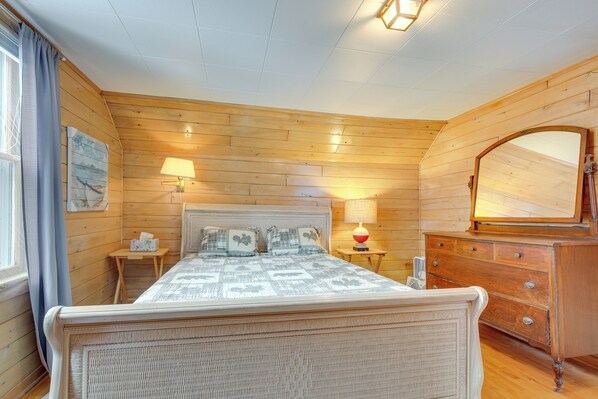 Un dormitorio con paneles de madera, una cama, mesitas de noche, un aparador y un espejo.