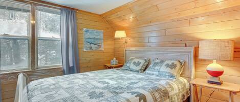 Une chambre confortable avec un plafond en bois, un grand lit recouvert d’une courtepointe, deux lampes de chevet et une fenêtre avec des rideaux.