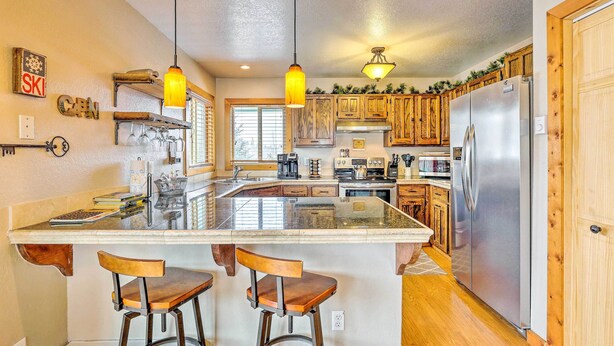 A kitchen with wooden cabinets, a stainless steel refrigerator, and a central island with bar stools. - Silverthorne Ski Base w/ Mtn Views: Walk to Trails (Silverthorne)