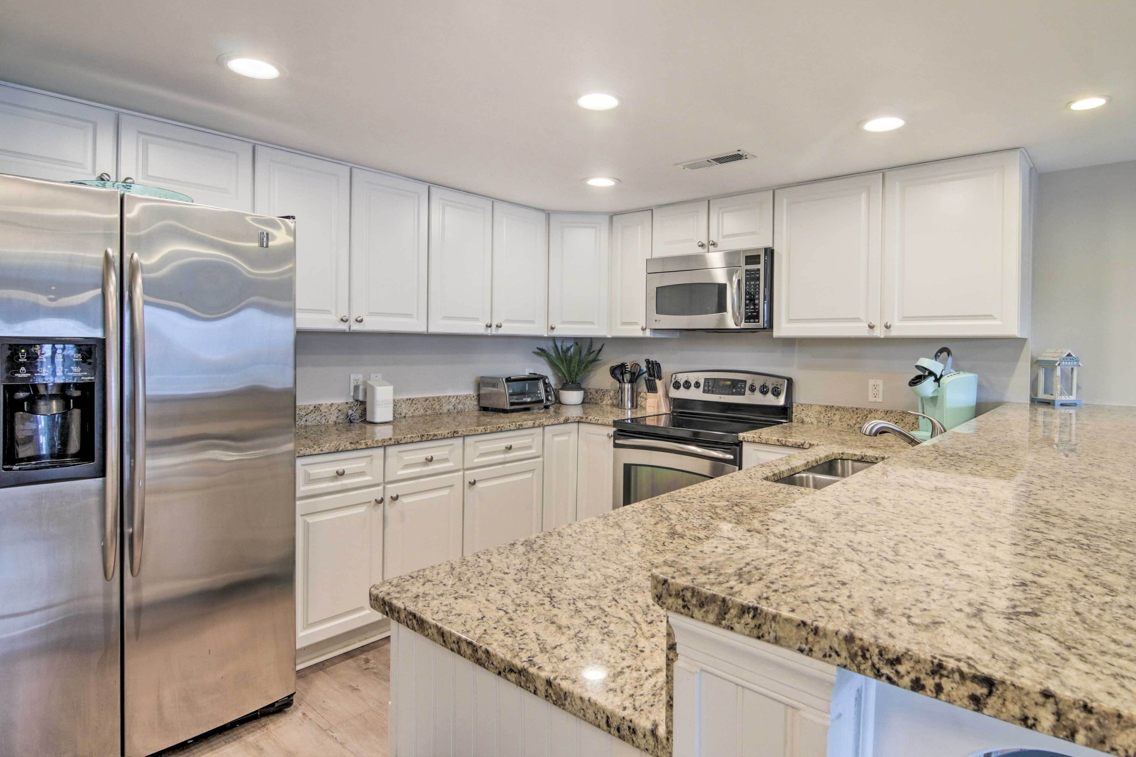 A modern kitchen with white cabinets, stainless steel appliances, granite countertops, and under-cabinet lighting.