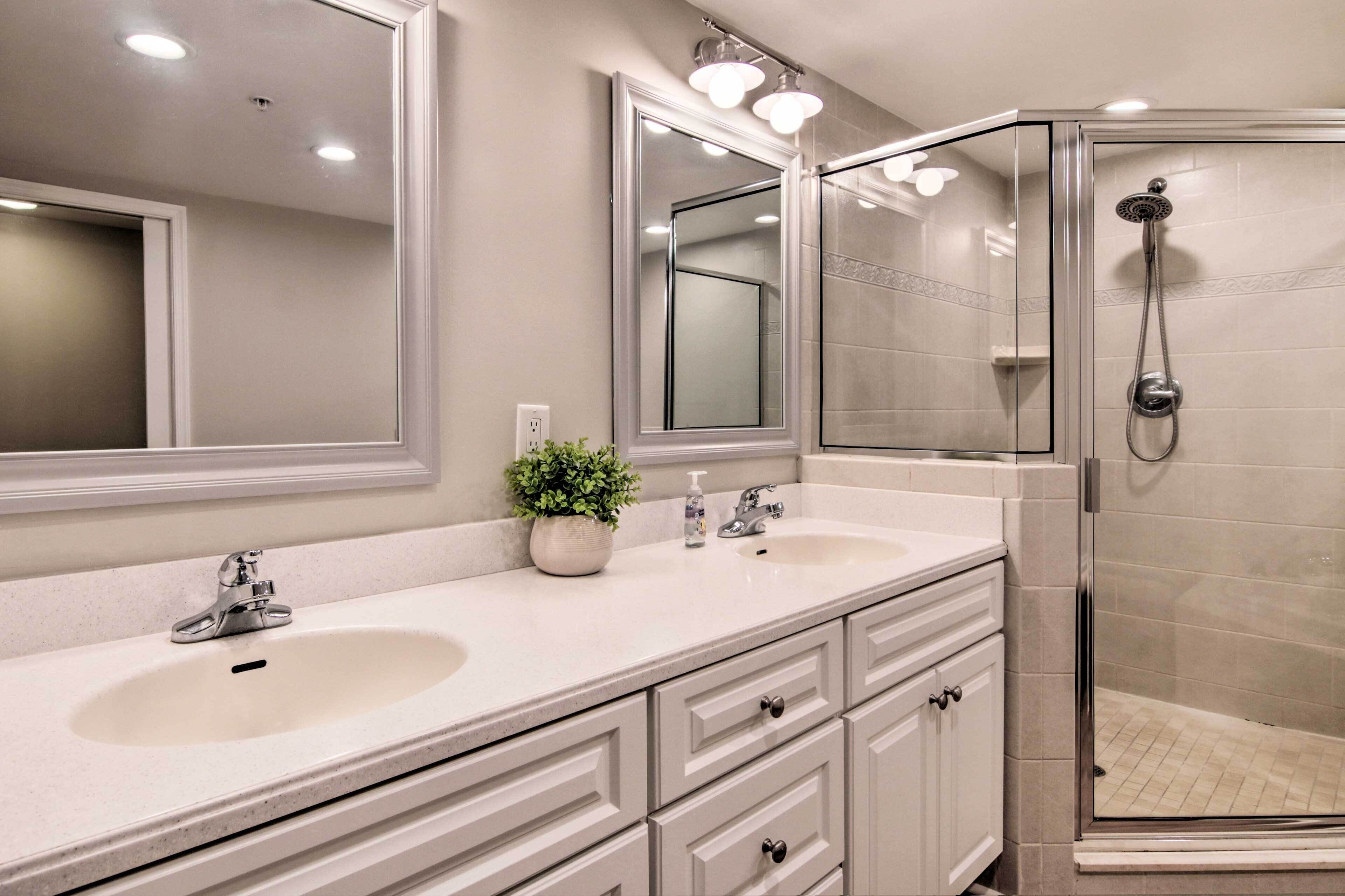 A bathroom with two sinks, a mirror, a potted plant, and a glass-enclosed shower.
