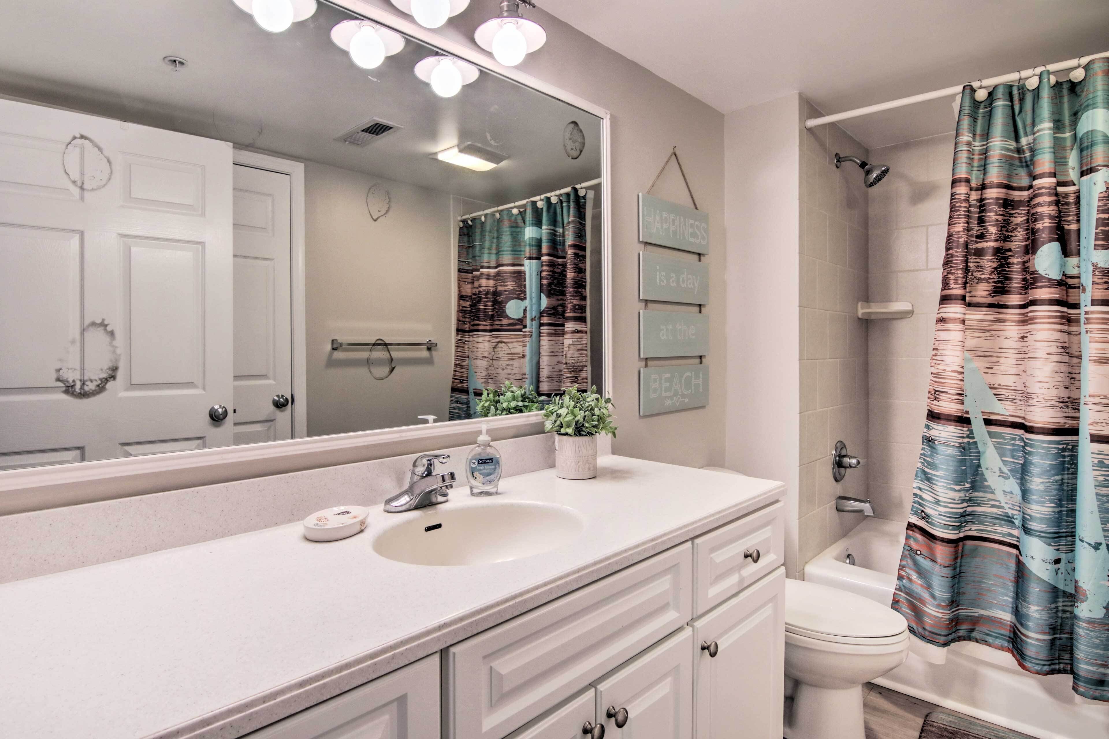 A bathroom with a white sink, mirror, and toilet. There is a shower curtain with a beach-themed design.