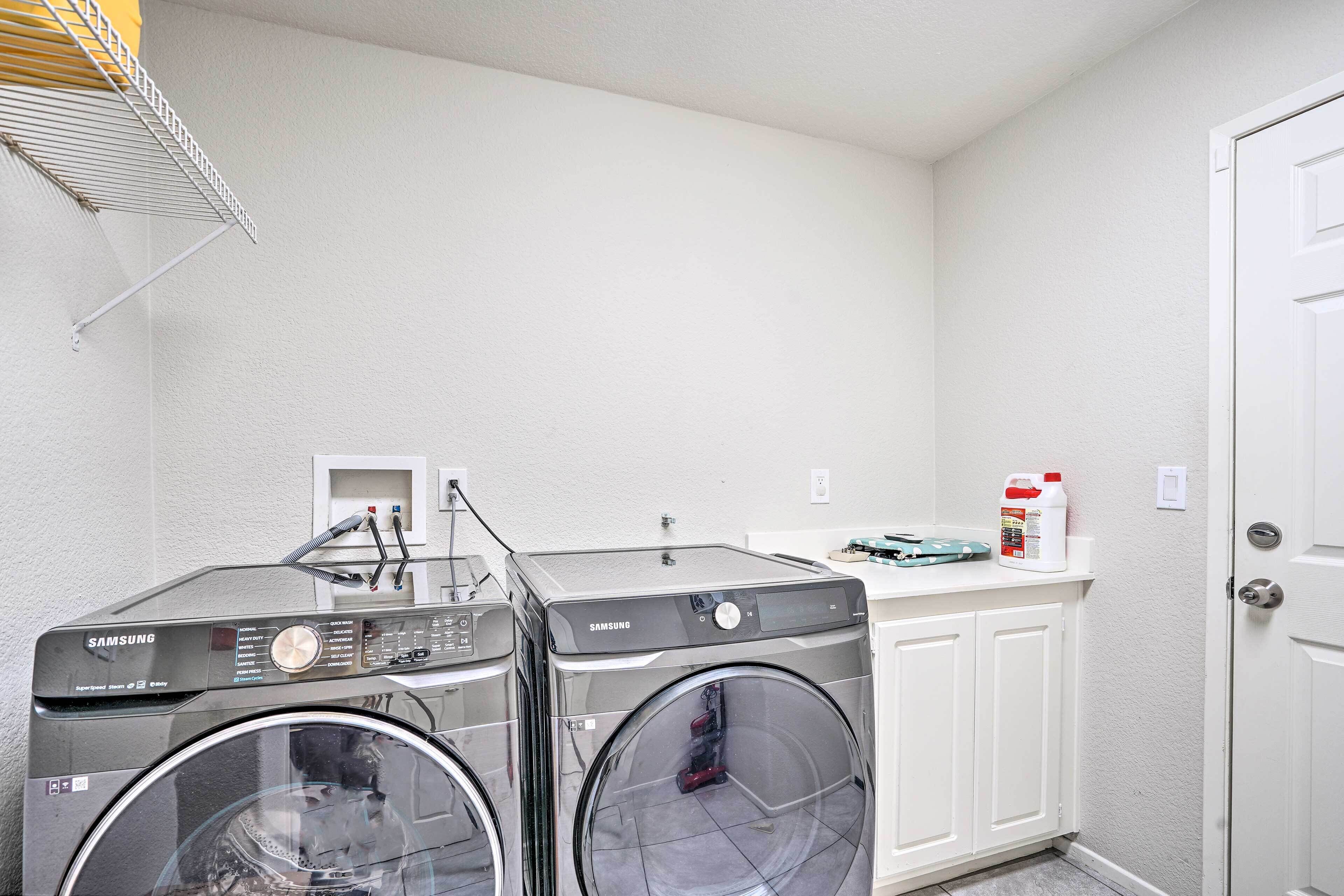 A laundry room with two Samsung front-loading washing machines, a white door, and a small shelf with cleaning supplies.