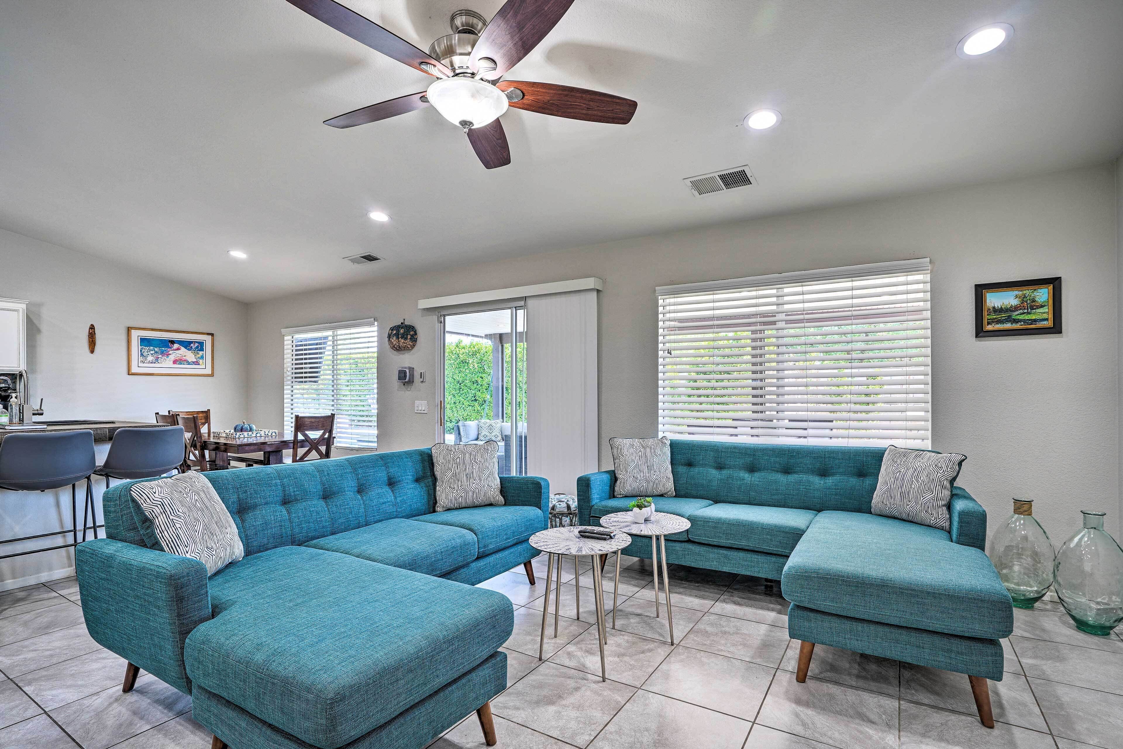 A modern living room with a sectional sofa, a ceiling fan, and a dining area with chairs and a table.
