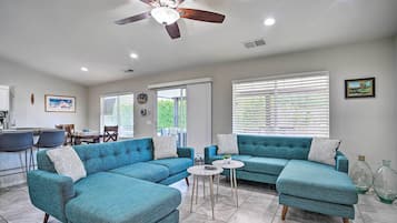 A modern living room with a sectional sofa, a ceiling fan, and a dining area with chairs and a table.