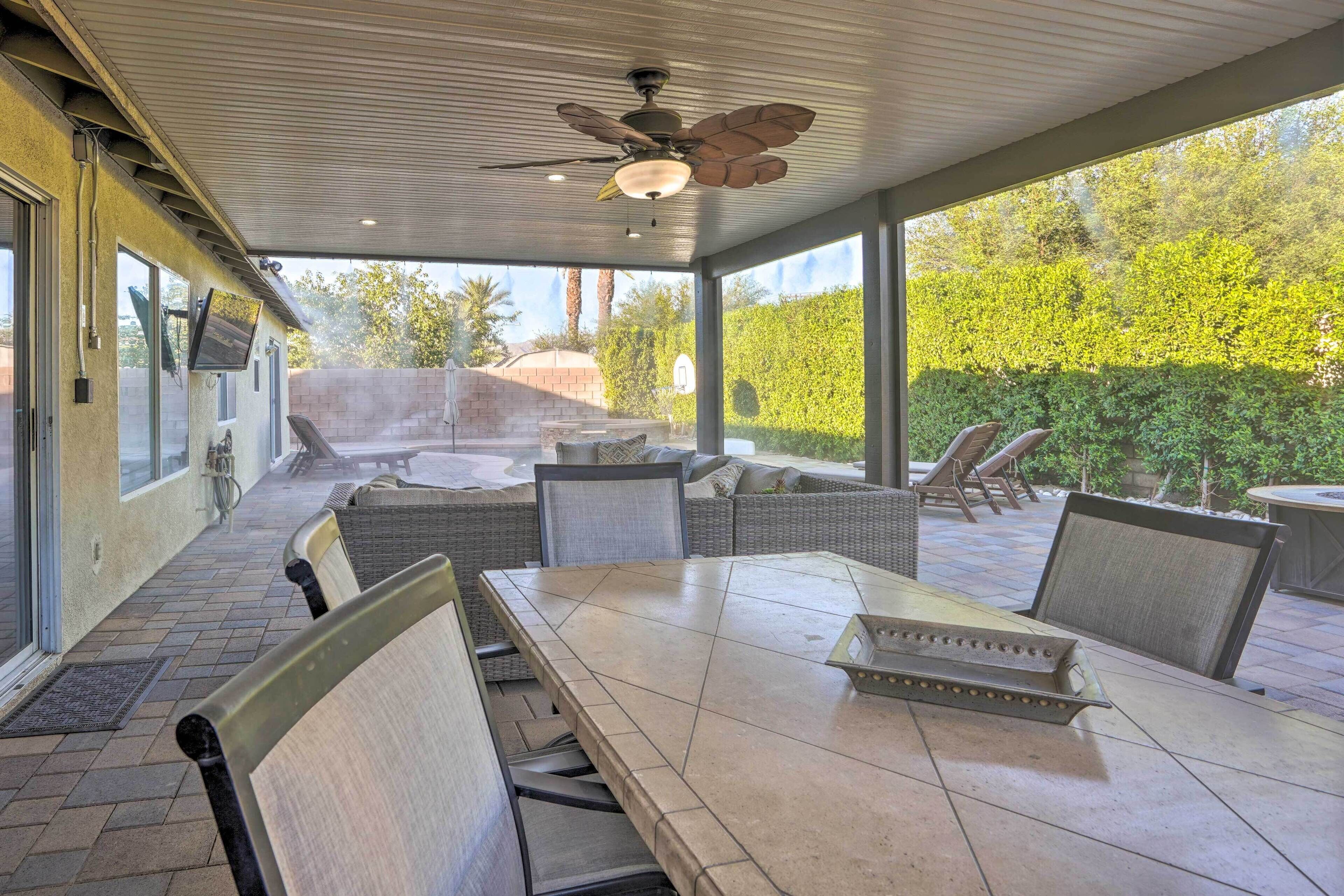A covered patio area with a dining table, chairs, and a ceiling fan.