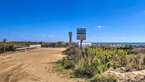 Una playa con un sendero de tierra que lleva a una cerca de madera y un cartel que indica un acceso a la playa.