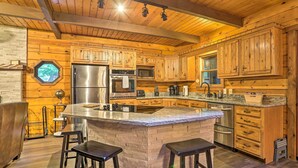 A spacious kitchen with wooden cabinets, a large island with stools, stainless steel appliances, and a unique octagonal window. - Pocono Log Cabin: Fireplace, Fire Pits & Amenities (Pocono Lake)