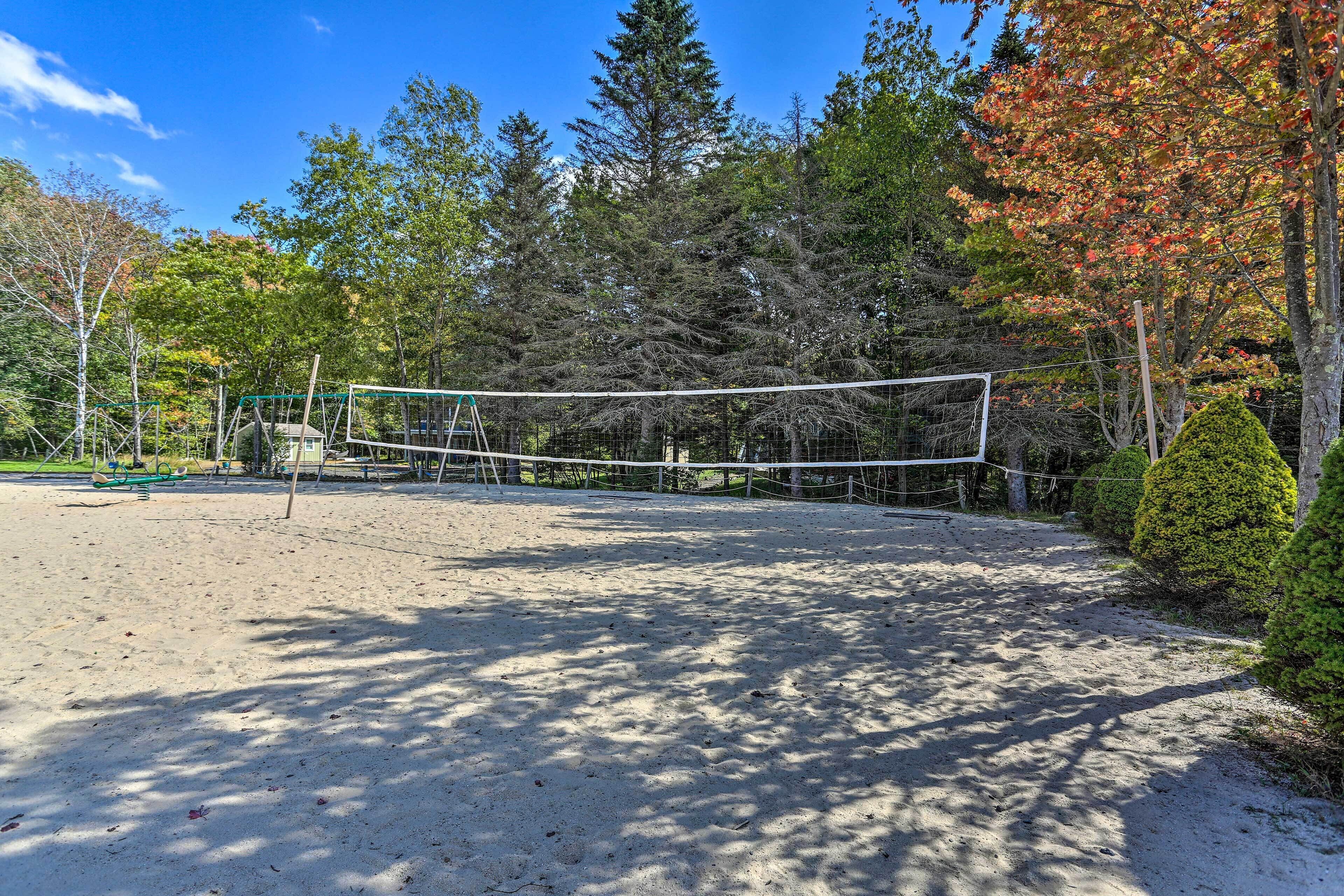 A sandy volleyball court surrounded by trees and a fence.
