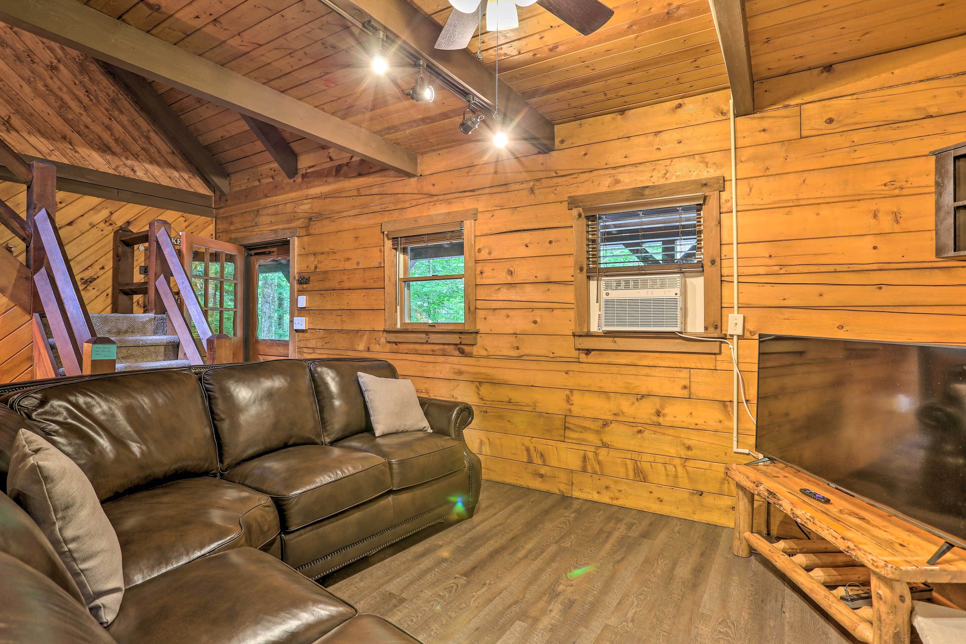 A wooden cabin interior with a leather sofa, wooden walls, and a ceiling fan.