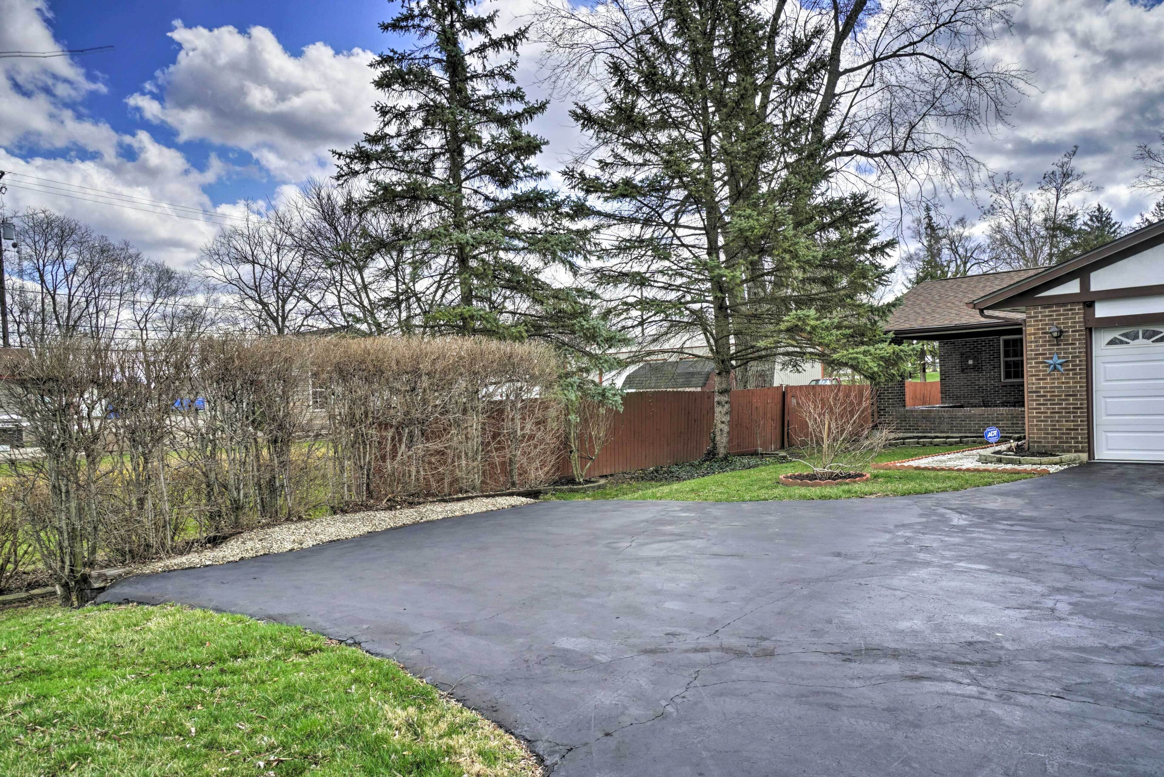 A residential driveway with a curved path leading to a garage. There are trees and a wooden fence in the background.