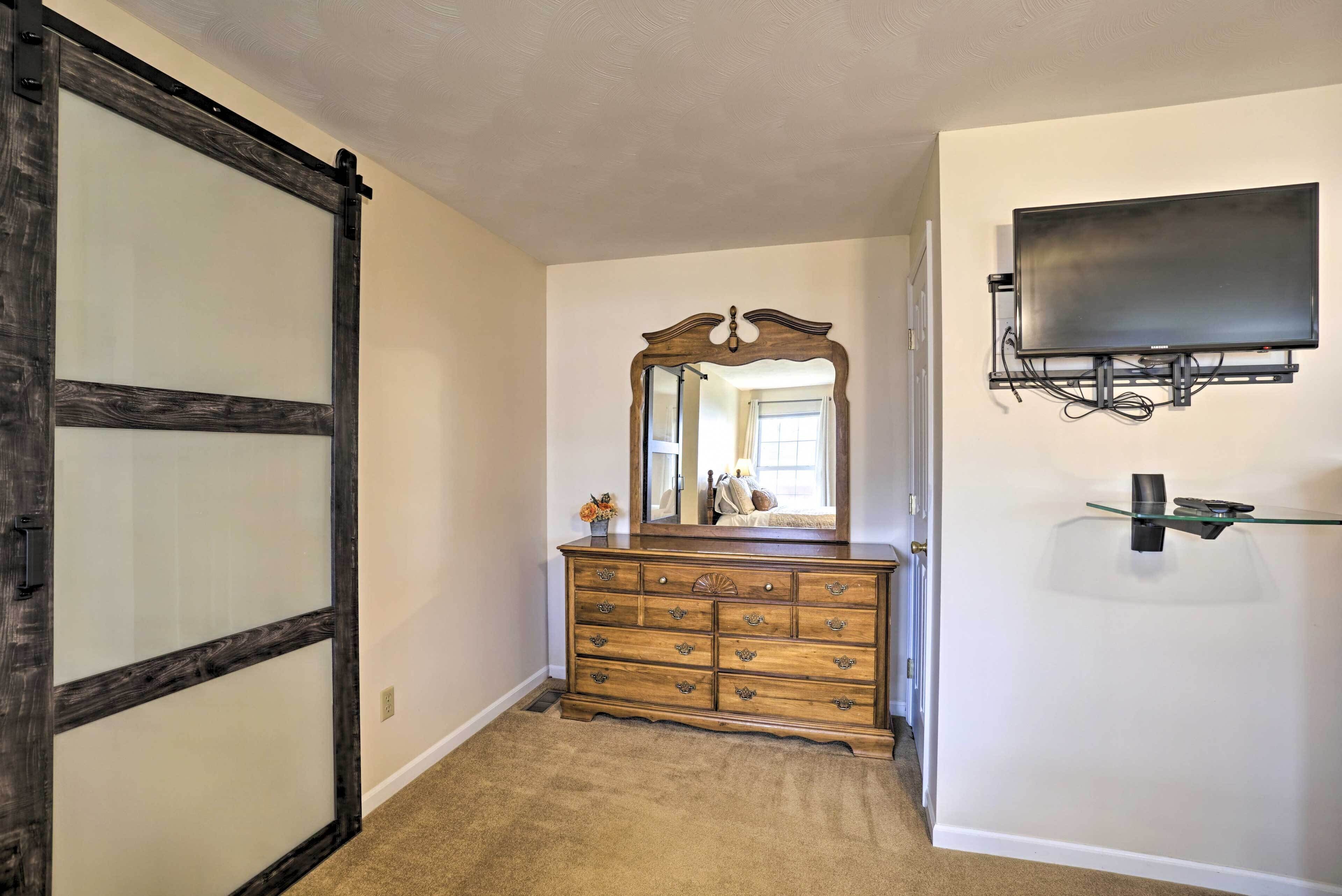 A bedroom with a wooden dresser, a mirror, a flat-screen TV mounted on the wall, and a sliding door.