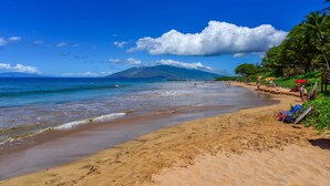Une plage avec une eau d’un bleu limpide, un rivage sablonneux et une montagne en arrière-plan.