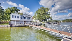 A house with a dock extending into a body of water, surrounded by trees and a clear sky. - Lake View Cottage: Lake Ozarks Getaway (Gravois Mills)
