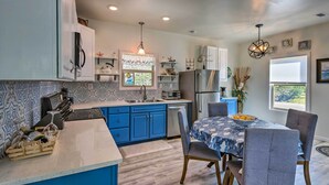 A modern kitchen with blue cabinets, a stainless steel refrigerator, and a dining area with a table set for four. - East Bay Vacation Rental w/ Dock! (Gulf Breeze)