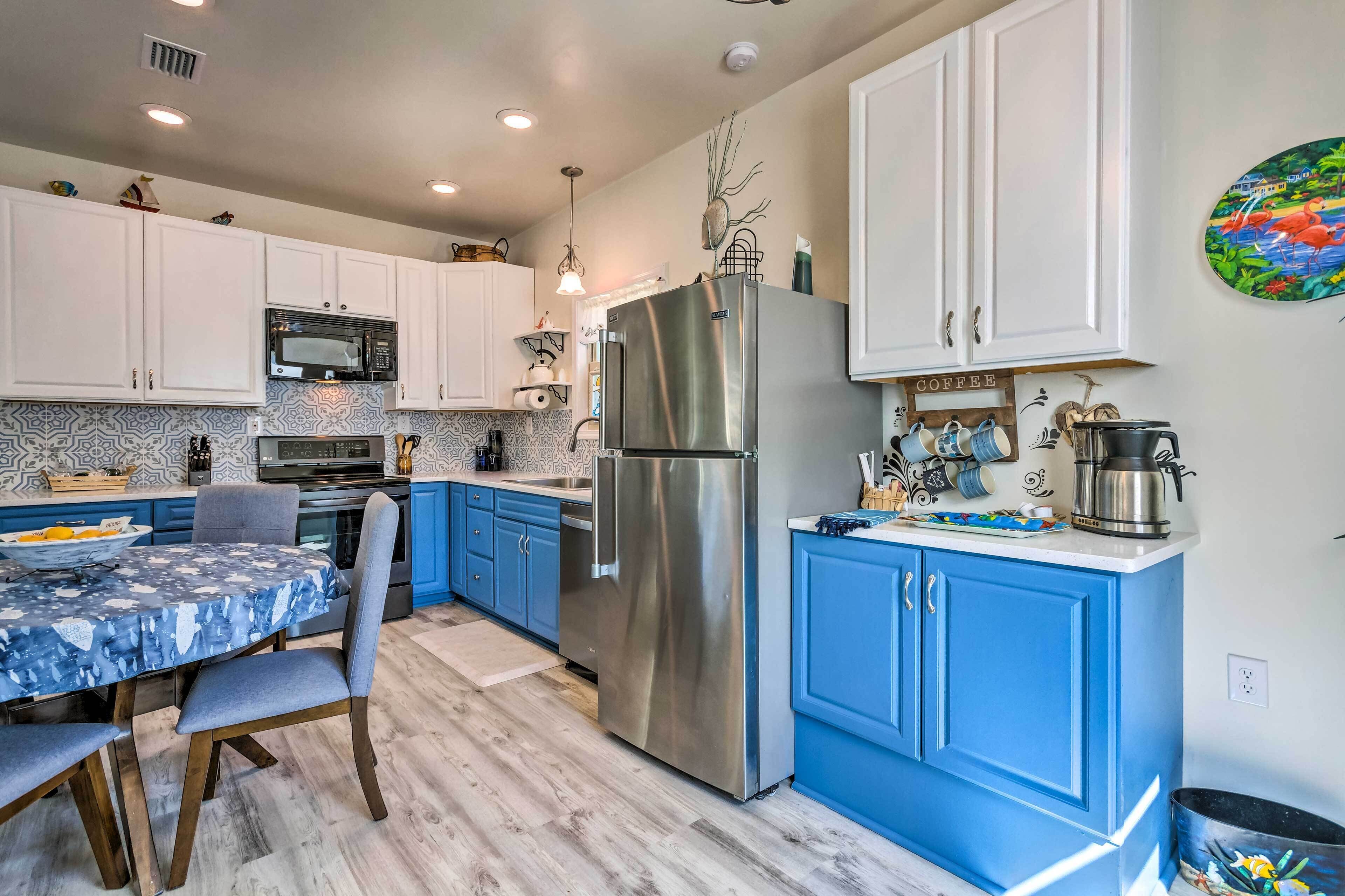 A modern kitchen with white and blue cabinets, stainless steel appliances, and a dining area with a blue tablecloth.