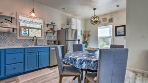 A modern kitchen with blue cabinets, a stainless steel refrigerator, and a dining area with a table covered in a blue and white patterned tablecloth. - East Bay Vacation Rental w/ Dock! (Gulf Breeze)